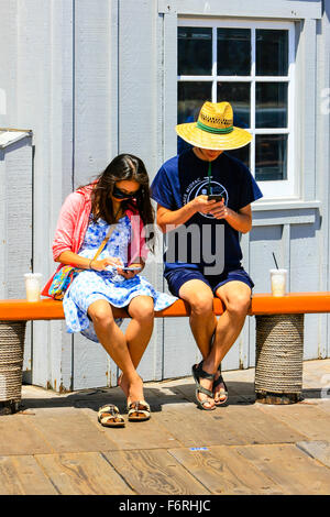 Two people sitting on a bench seat interacting with their cellphones but ignoring each other Stock Photo