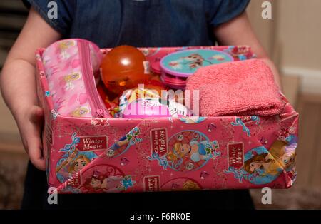 A three year old girl carrying a charity appeal shoe box with presents for a girl Stock Photo
