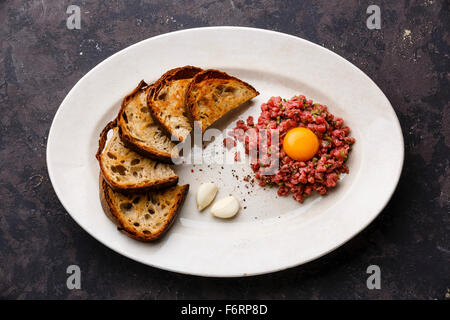 Beef tartare with pickled cucumber and toasts on white plate on dark background Stock Photo