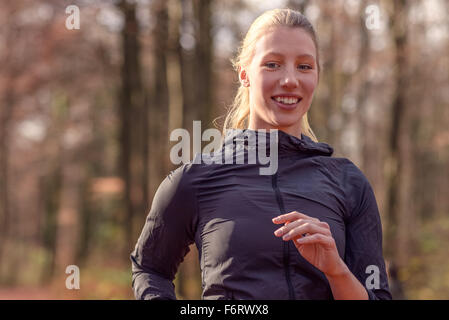 Pretty fit young woman jogging through autumn or fall woodland approaching the camera, close up upper body portrait in a healthy Stock Photo