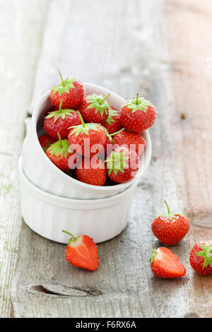 White Ramekins filled with succulent juicy fresh ripe red strawberries on an old wooden textured table top Stock Photo
