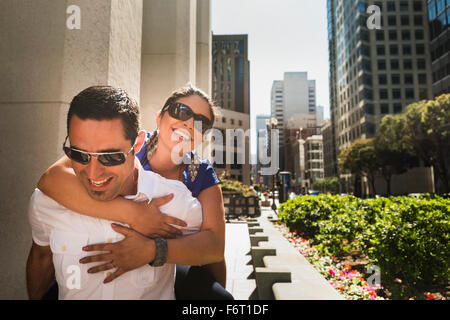 Hispanic man carrying girlfriend piggyback in city Stock Photo