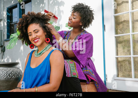 Woman combing hair of friend on porch Stock Photo