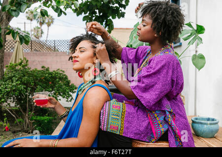 Woman combing hair of friend on front stoop Stock Photo