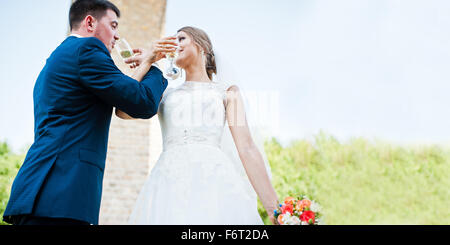 fashionable and happy wedding drinking champagne from glasses under stone bridge Stock Photo