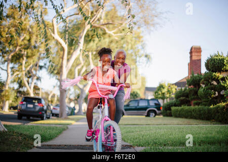 Mother pushing daughter on bicycle Stock Photo