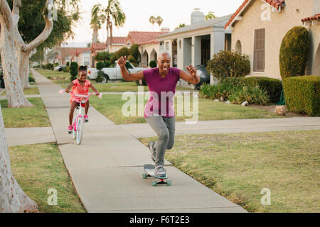 Mother and daughter riding skateboard and bicycle on sidewalk Stock Photo