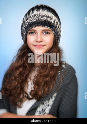 Portrait of cute teen girl wearing stylish knitted hat and sweater isolated on blue background, winter fashion for teenagers Stock Photo