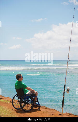 Disabled man in wheelchair fishing on beach Stock Photo