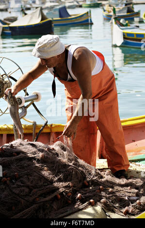 Maltese fisherman taking out fish from fishing net on a boat in the harbour of Marsaxlokk, Malta Stock Photo
