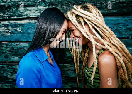 Smiling women touching foreheads at wooden wall Stock Photo