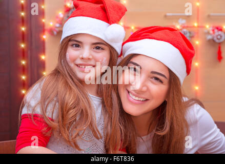 Closeup portrait of mother with cute little daughter wearing Santa hat baking on the kitchen at home, enjoying Christmas Stock Photo