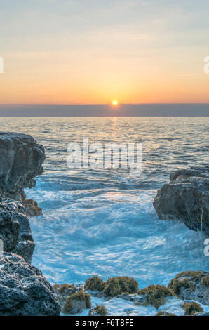 Sunrise over rock formations on beach Stock Photo
