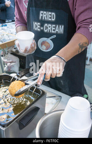 young man lifts golden ball of fried ice cream out of deep fryer at street fair on Broadway closed to traffic on autumn Saturday Stock Photo