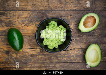 Bowl of Guacamole and whole and sliced avocados on dark wood Stock Photo