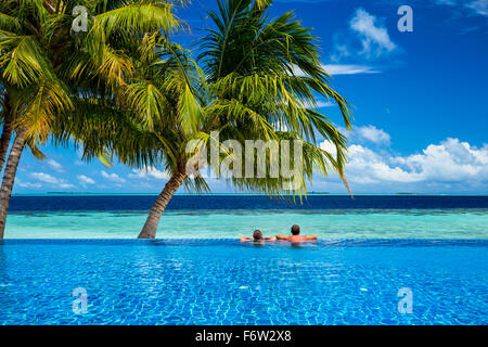 young couple relaxing in infinity pool under coco palms in front of tropical  landscape Stock Photo