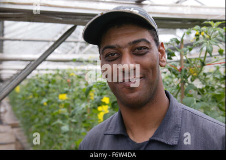 Portrait of man with learning disability standing in greenhouse at Brook Farm; Linby; wearing cap and smiling, Stock Photo