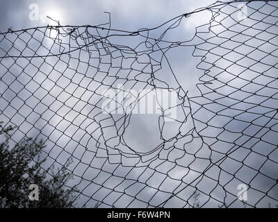 Patched hole in wire mesh fence. Grey day. Stock Photo