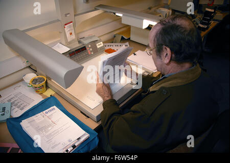 Man with disability working as microfilm technician; sitting at desk in visual communications office organising papers, Stock Photo
