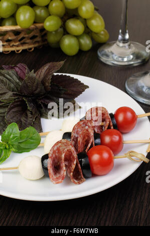 Appetizer of salami with mozzarella, olives, cherry tomatoes on skewers with basil Stock Photo