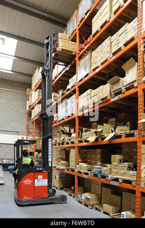 a compact, high-reach fork lift truck removes goods on a pallet from high-level racking  in a modern storage warehouse Stock Photo