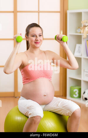 Pregnant woman doing fitness exercises sitting on gym ball working out with dumbbells Stock Photo