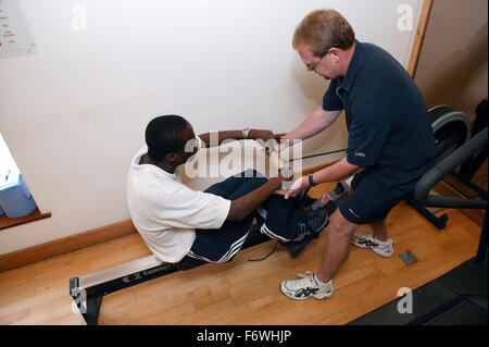 Access to services,  Fitness instructor and disabled man in the gym; using Rowing Machine, Stock Photo