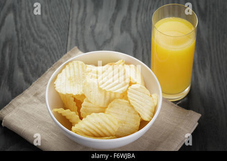 rippled organic chips in white bowl wit orange juice Stock Photo