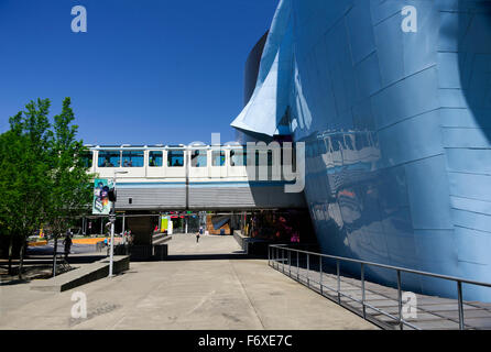 Seattle Center Monorail Skytrain comes out of EMP Museum heading for the Space Needle at Seattle Centre; Seattle, Washington, United States of America Stock Photo