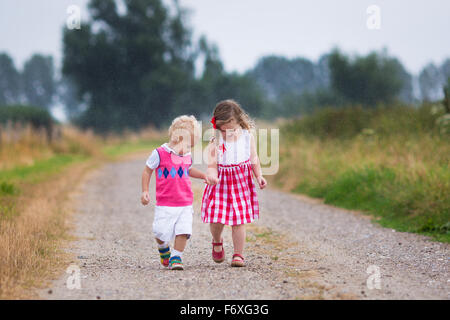 Girl and boy playing in the rain. Kids play outdoor by rainy weather in fall. Autumn fun for children. Toddler kid and baby walk Stock Photo