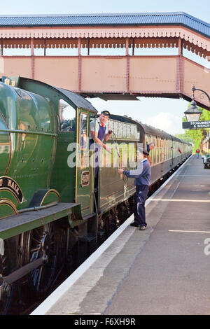 The signalman exchanges a single line token with the fireman of steam train at Williton station on the West Somerset Railway, En Stock Photo