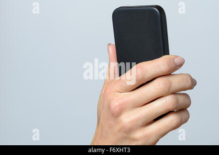 Hand holding a black cellular Against Gray Background with Copy Space. Stock Photo