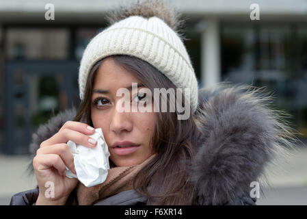 Sad tearful woman in warm winter fashion holding a handkerchief to her face to dry the tears from her eyes looking into the came Stock Photo