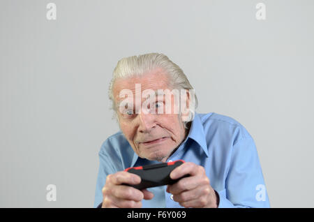 Funny elderly man or grandfather playing a video game on console, portrait with copy space on gray Stock Photo