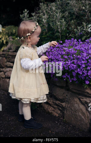 Toddler girl in dress looking at spring flowers in garden Stock Photo