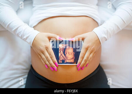 Pregnant woman holds ultrasound photo on the belly in bed Stock Photo