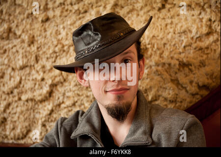 Young man in tip hat portrait, smiling adult European man with small beard sitting in bar in a dark brown Australian theme hat Stock Photo