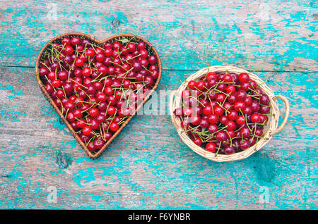Fresh cherries in wicker baskets on painted wooden rustic background Stock Photo