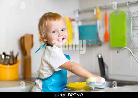 Toddler child washing dishes in kitchen. Little boy having fun with helping to his mother with housework. Stock Photo