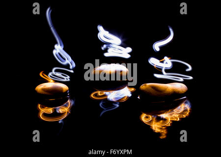 Light painting with three pebbles on water and black background. Stock Photo