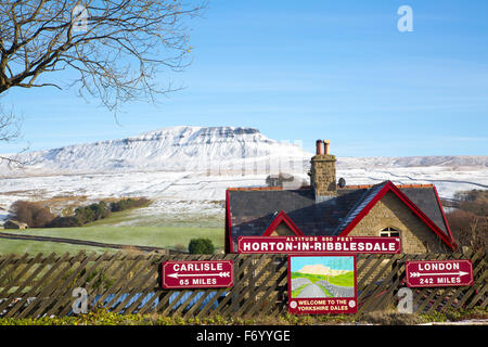 Horton in Ribblesdale railway station with signpost to Carlisle and London, with a snow covered Pen-y-ghent mountain behind Stock Photo