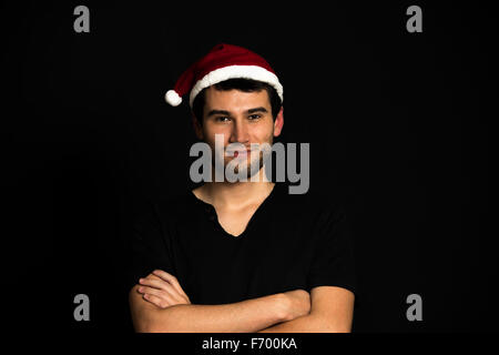 Young handsome brunette man wearing red hut, black t-shirt, smiling, happy, on black background low-key Stock Photo