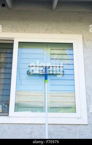 Window washer uses a sponge and squeegee on a pole to wash the exterior windows of a home. Stock Photo