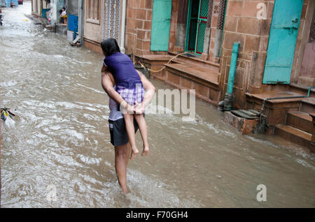 Man carrying daughter on back rain water on street, jodhpur, rajasthan, india, asia Stock Photo