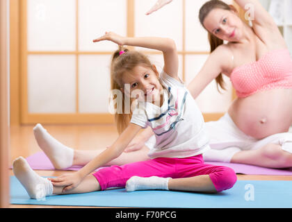 Cute pregnant mother and daughter doing exercise at home Stock Photo