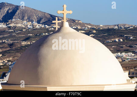 Santorini. Two white washed domes of a Greek orthodox church, one behind the other, both with crosses on. Background mountains and scattered buildings. Stock Photo