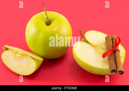 Fresh apples and cinnamon sticks with a ribbon on red background Stock Photo