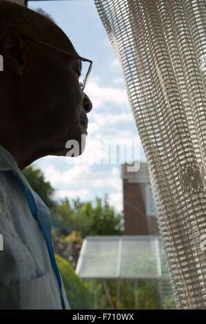 Older man looking out of the window through a curtain, Stock Photo