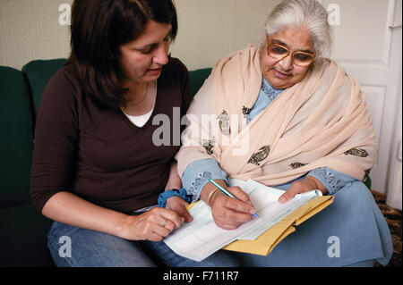 Community support worker helping South Asian lady fill in a form, Stock Photo