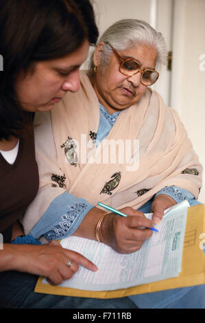 Community support worker helping South Asian lady fill in a form, Stock Photo
